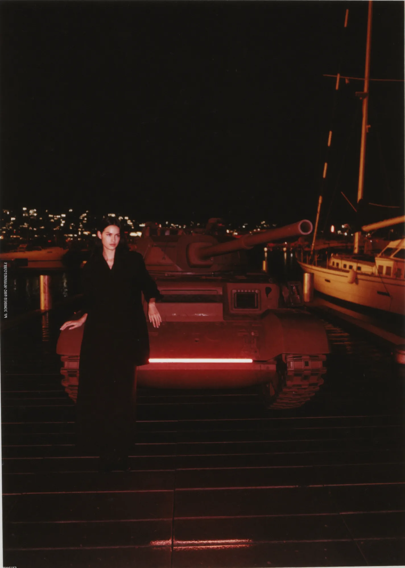 Figura de noche en un muelle, embarcación con luz roja y veleros al fondo