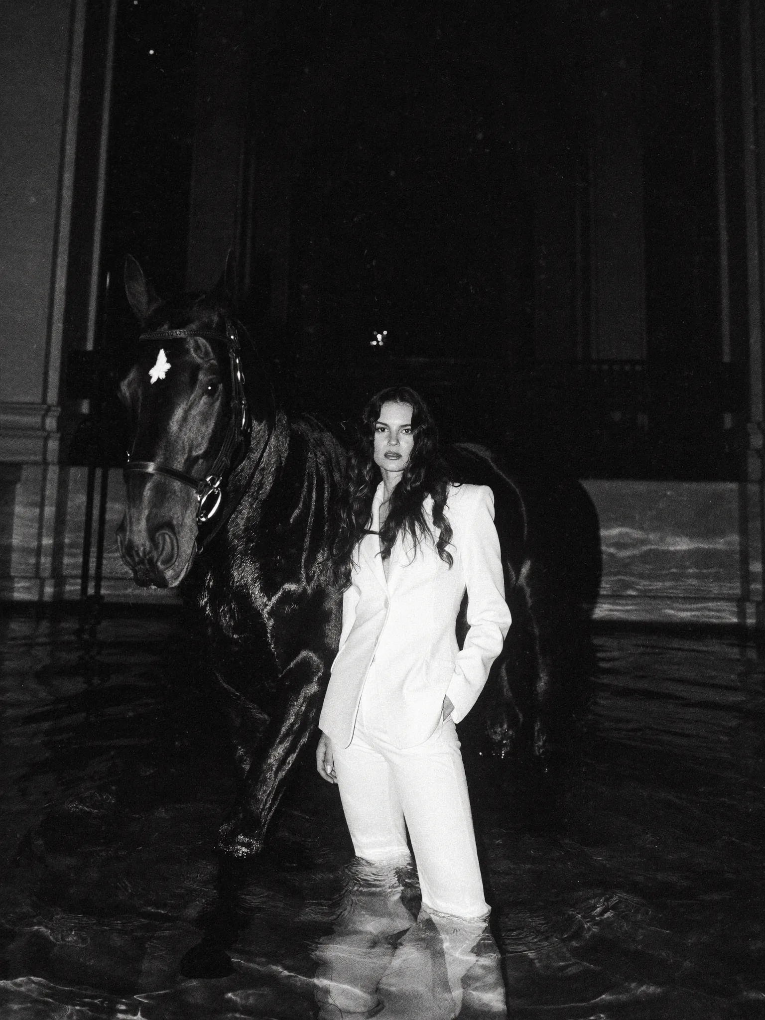 Traje blanco y caballo negro en agua, escena nocturna